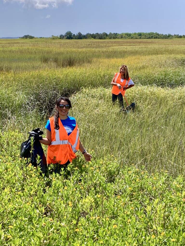 two women in marsh picking up litter. 