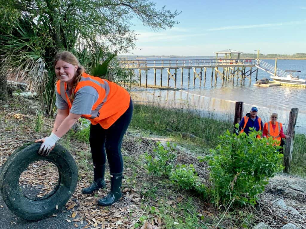 woman pulling tire out of marsh with dock behind.