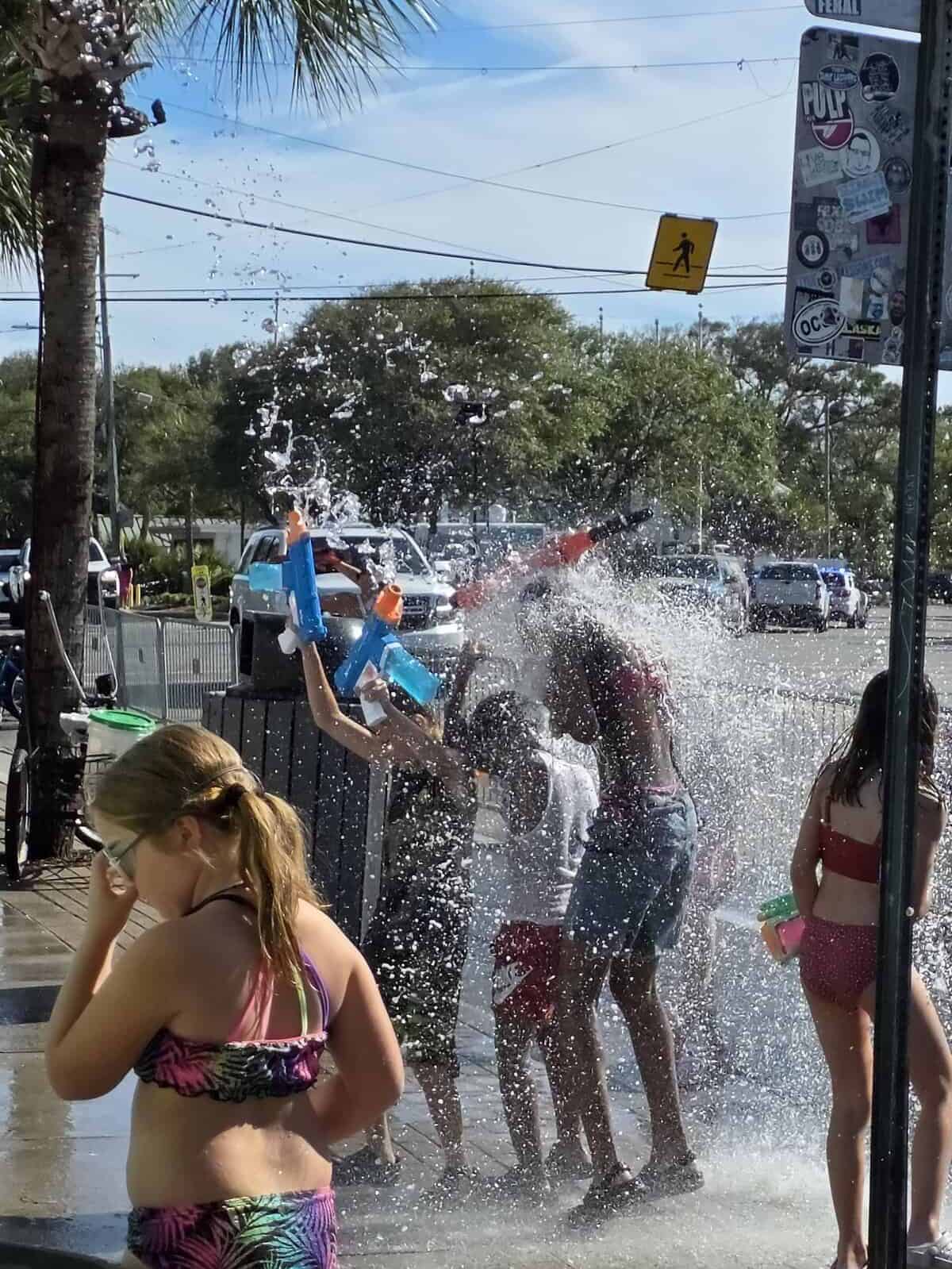 Kids holding water guns in the air are doused with a bucket full of water on a Tybee Island sidewalk at the Beach Bum Parade.